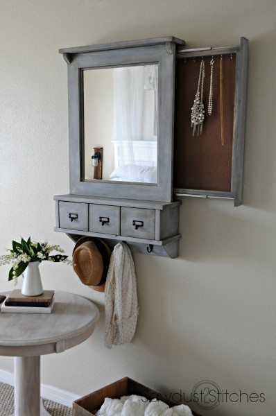 A framed mirror hides a slide out compartment that holds a jewelry collection behind.