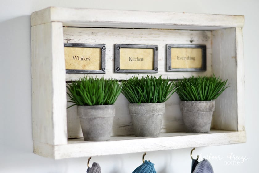 DIY wall shelf with hooks holding cleaning cloths and labels that say "window, kithen, everything"