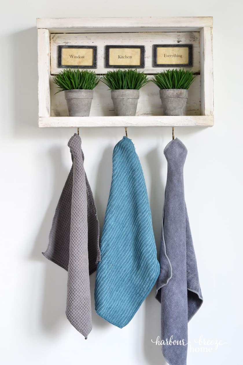 Rustic wall shelf with hooks holding Norwex cleaning cloths.