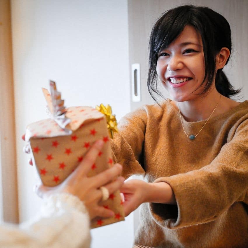 A lady handing over a gift for a Christmas gift exchange game.