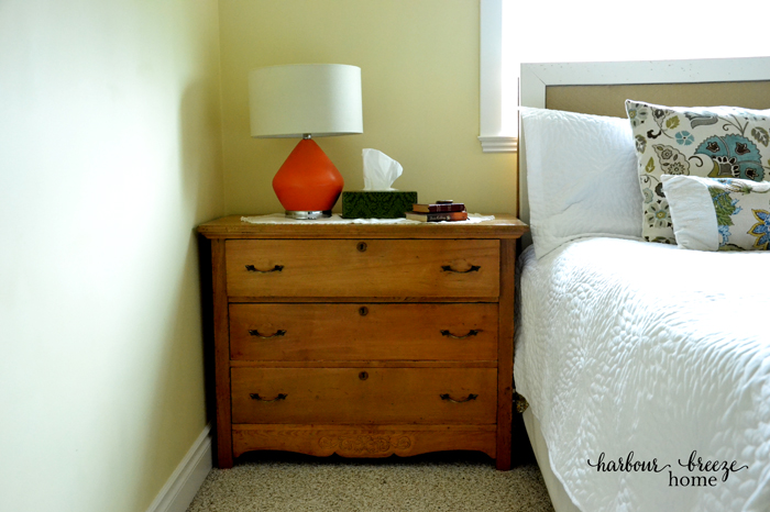 A small chest of drawers beside the bed that acts as storage and a nightstand.