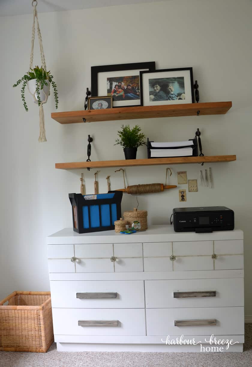 A dresser with floating shelves above it with office supplies - like a printer, desktop file, and trays of printer paper sitting neatly on them.