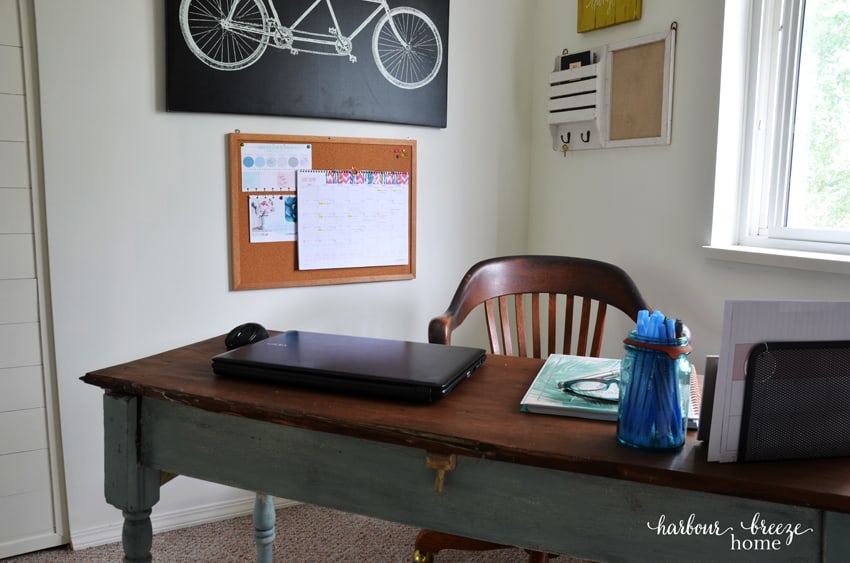 A bulletin board hanging above a desk with papers hung on it.