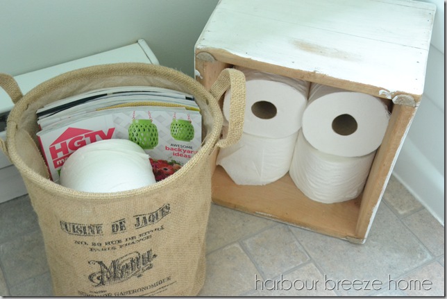 toilet paper rolls tucked into a basket and crate sitting on a bathroom floor.
