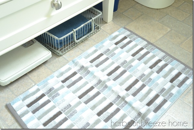 a weigh scale and a basket with towels tucked under a bathroom vanity.
