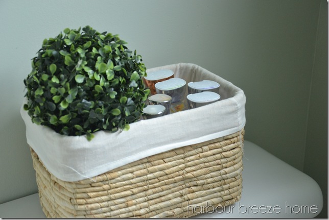 A lined wicker basket on the back of the toilet with lotion bottles in it.