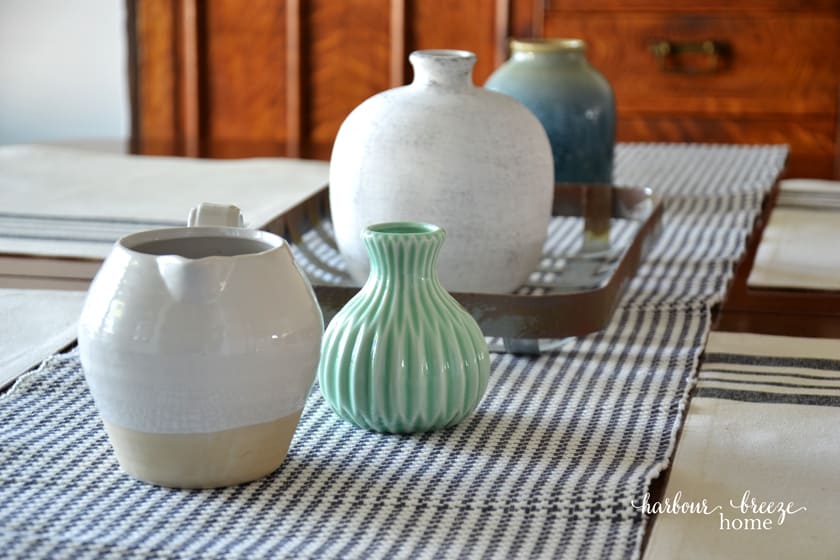 Empty vases and pitchers scattered down the center of a gray checked table runner
