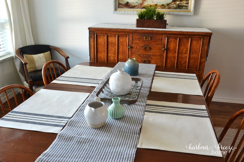 4 placemats with gray stripes sitting on a wooden table with a gray checked runner down the center
