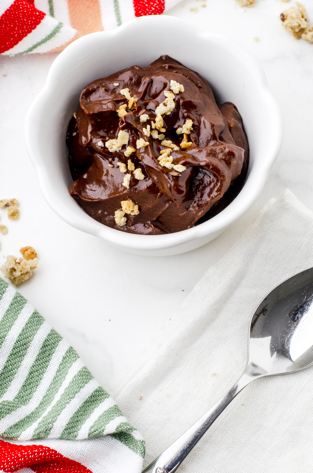 a bowl of chocolate avocado pudding with granola sprinkled on the top.