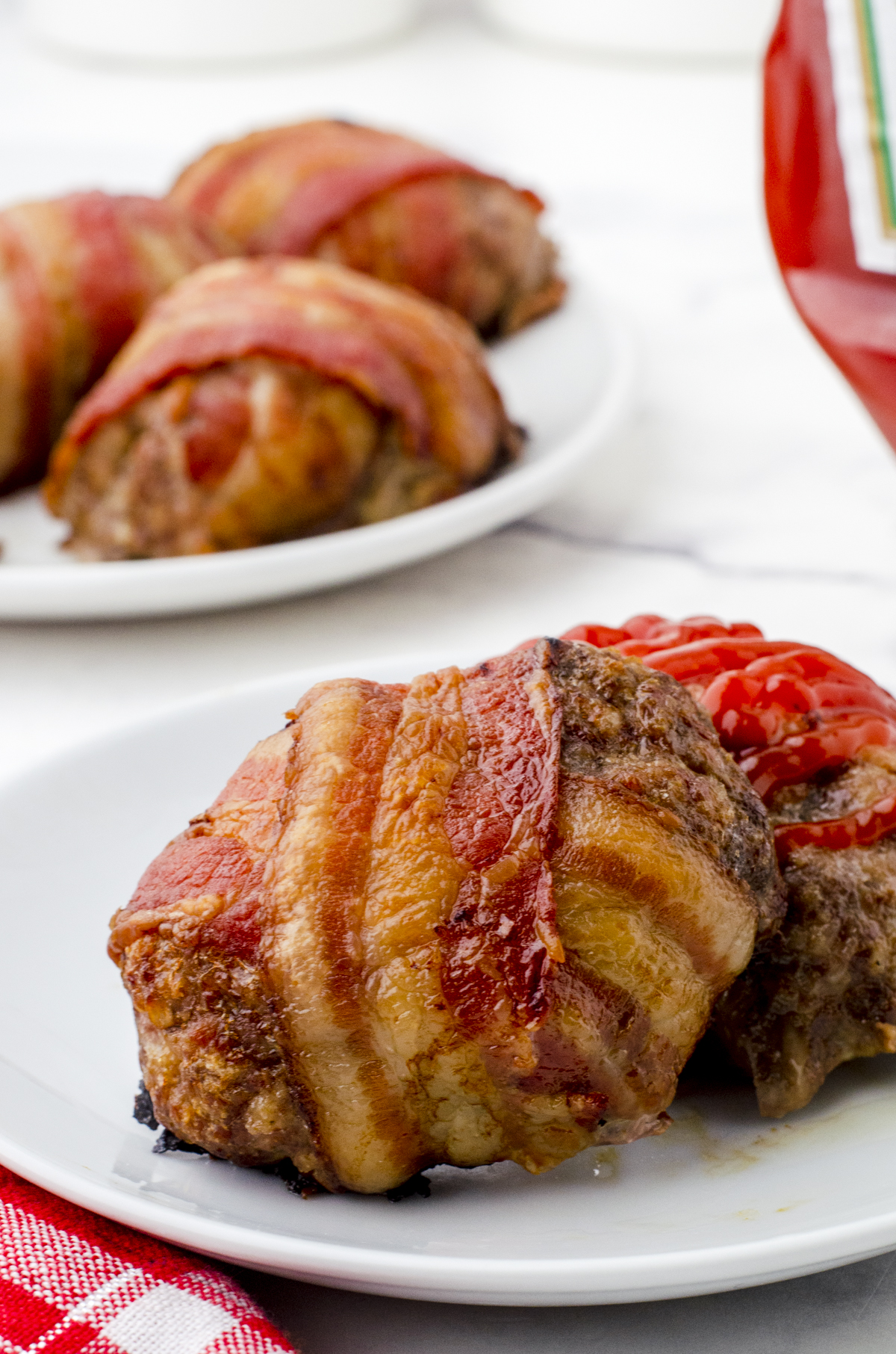 Bacon wrapped meatloaf on a plate ready to be eaten with a drizzle of ketchup on top.