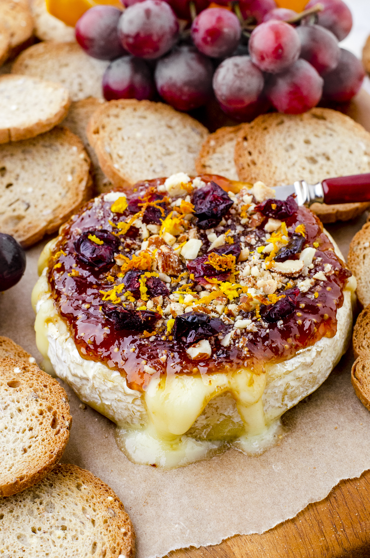 baked brie on a charcuterie board with crackers and grapes behind it