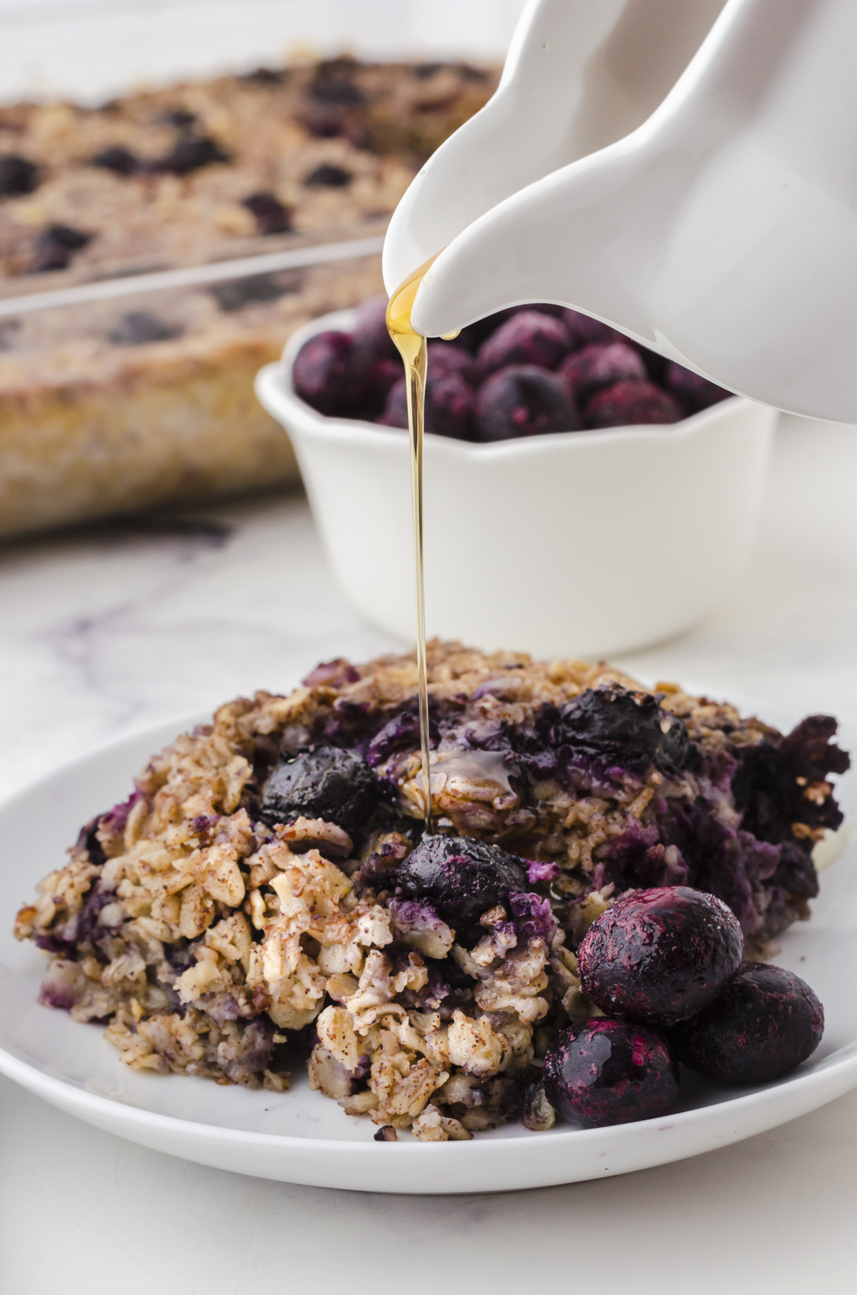 A piece of banana blueberry baked oats on a place with maple syrup being drizzled over the top.