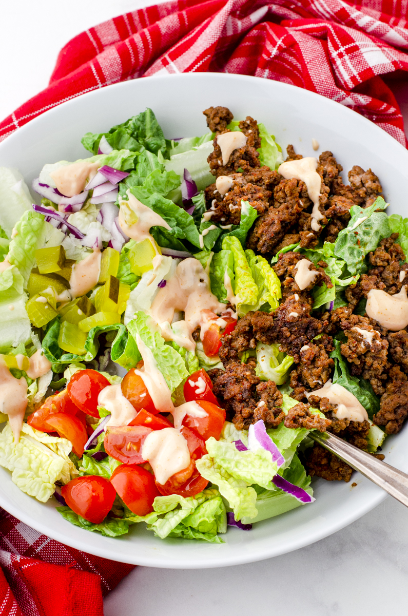 A healthy big mac salad bowl with special sauce drizzled on the top in a bowl ready to eat.