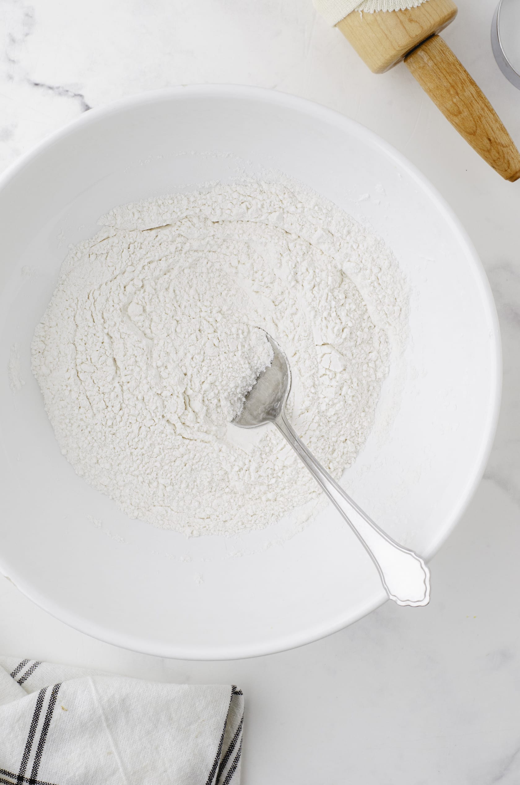 Dry ingredients for baking powder biscuits being mixed in a large white mixing bowl.