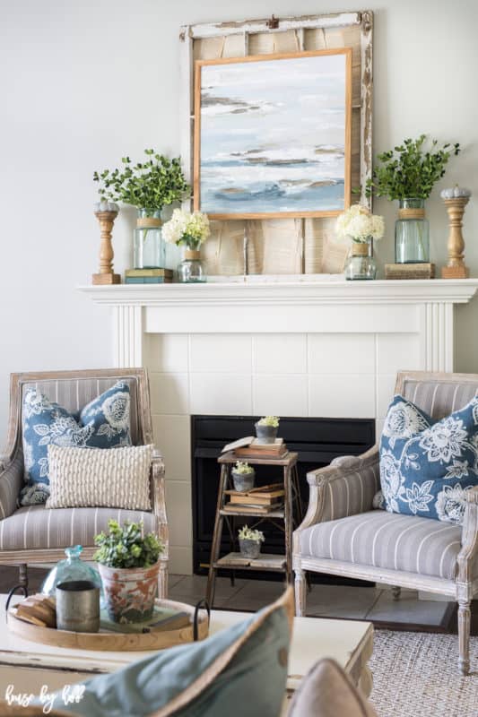 a fireplace mantle with a picture above it and 2 chairs flanking it with blue pillows for blue fall decor