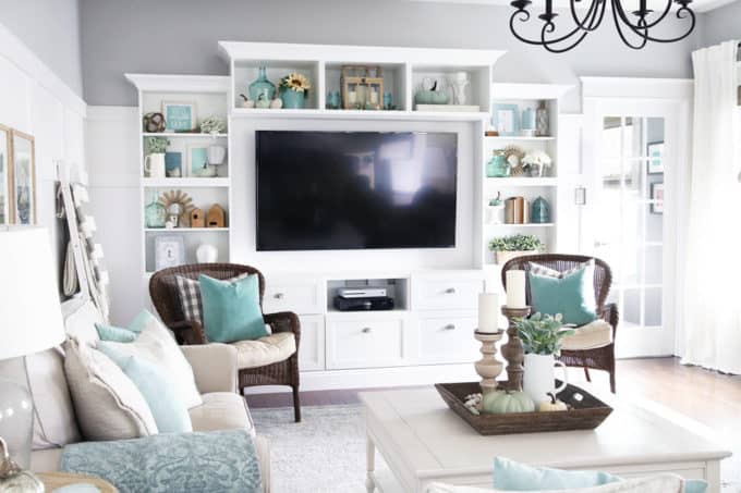 a built in bookcase in a living room decorated with a variety of blue fall decor pieces.