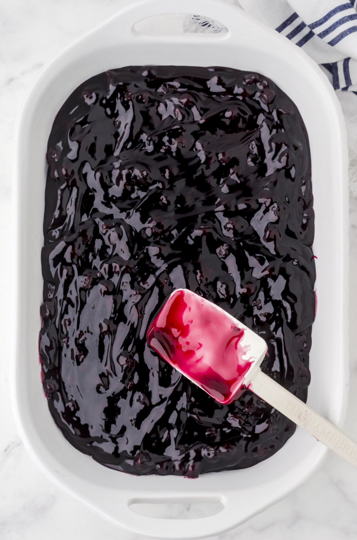 Blueberry pie filling in the bottom of a white baking dish for blueberry dump cake.