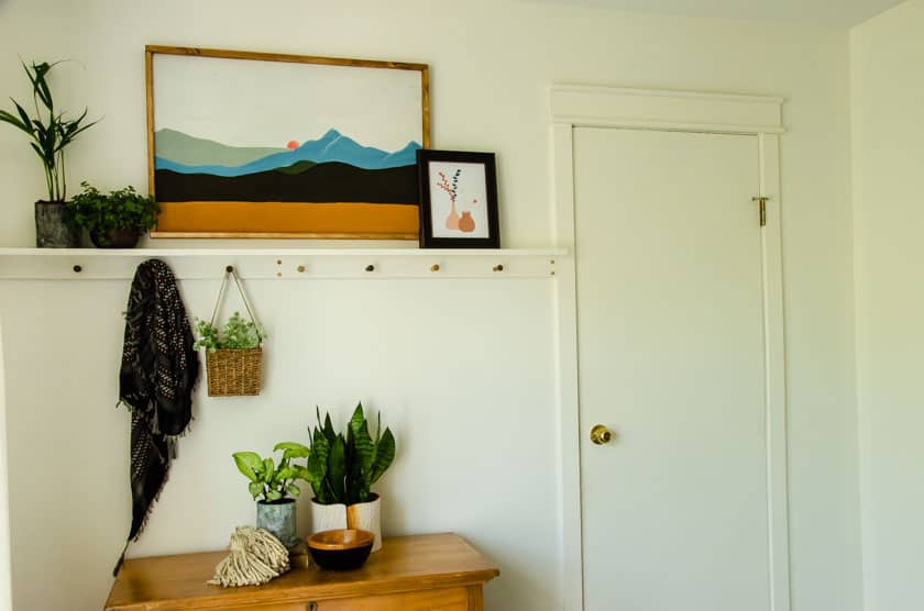 A boho shelf with pegs underneath above a dresser in a boho style bedroom.