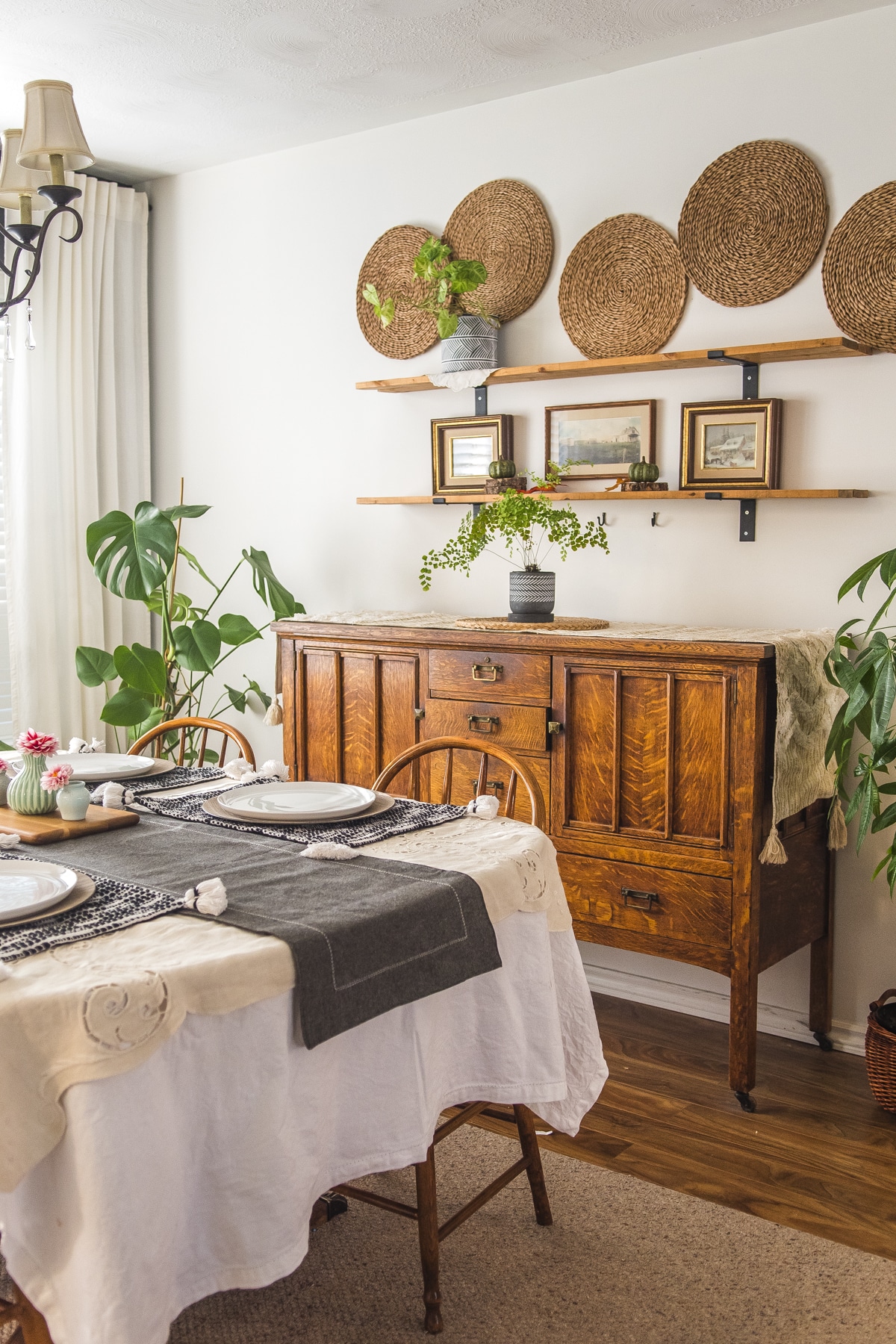plants around an antique buffet with farmhouse shelves above it with vintage pictures and plants on the shelf