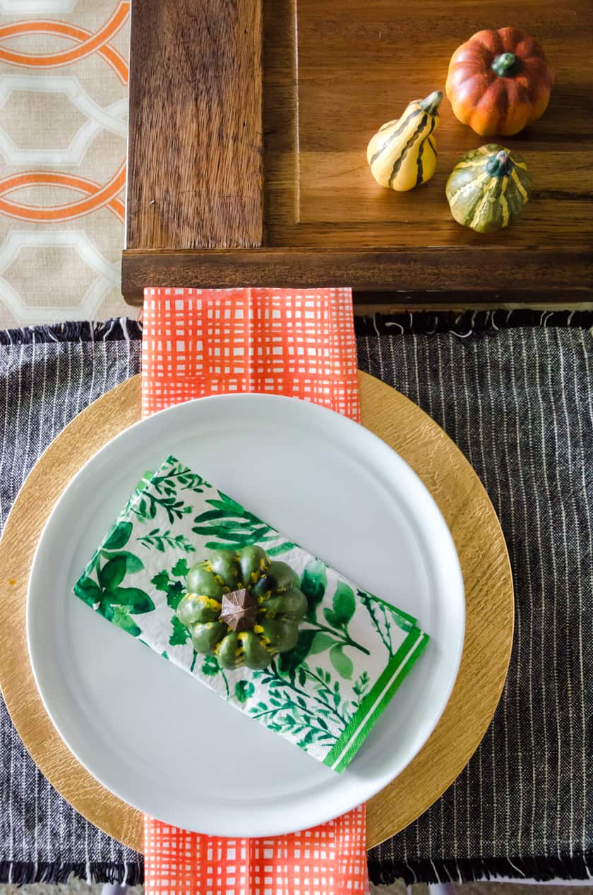 boho style table setting with a faux pumpkin sitting on a green floral napkin on a white plate