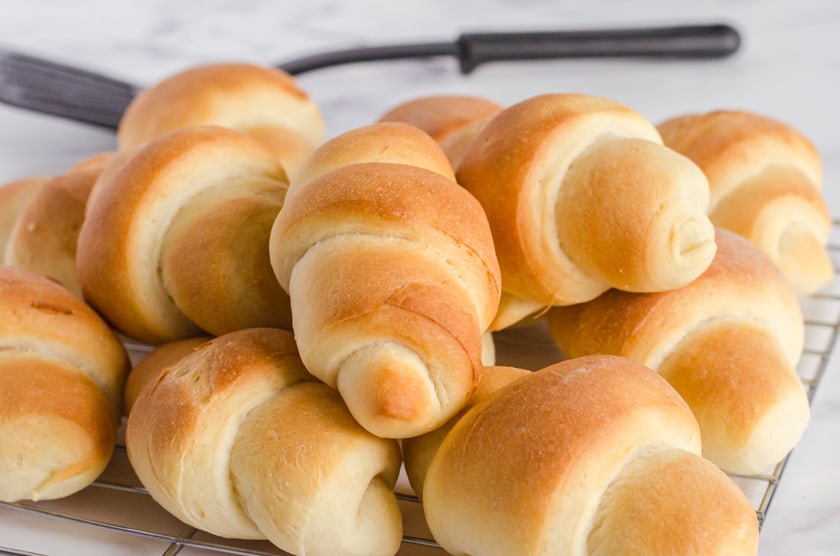 Crescent shaped homemade bread machine dinner rolls piled on a cooling rack.