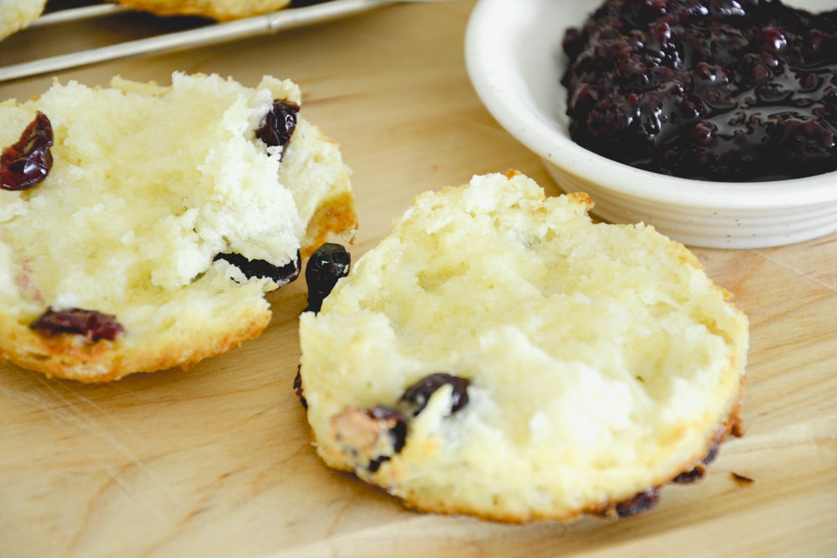 A split cranberry scone with a bowl of jam beside it.