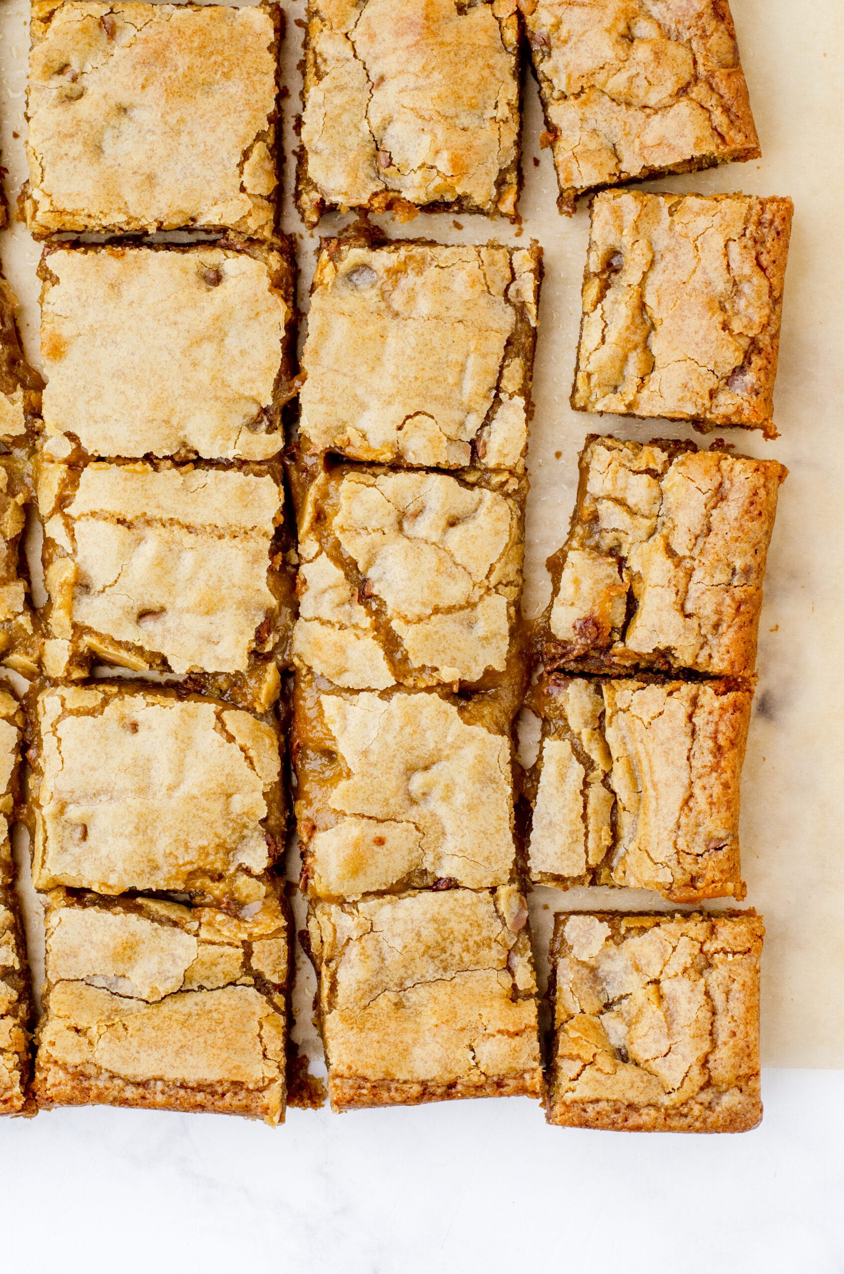 Butterscotch brownies cut and laying on a piece of parchment paper.