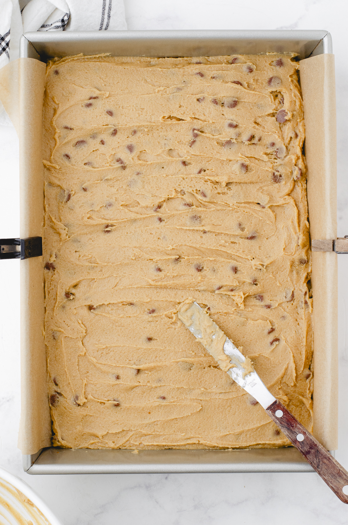 butterscotch brownie batter smoothed into the bottom of a parchment lined 9 x 13 inch baking pan and ready to go in the oven