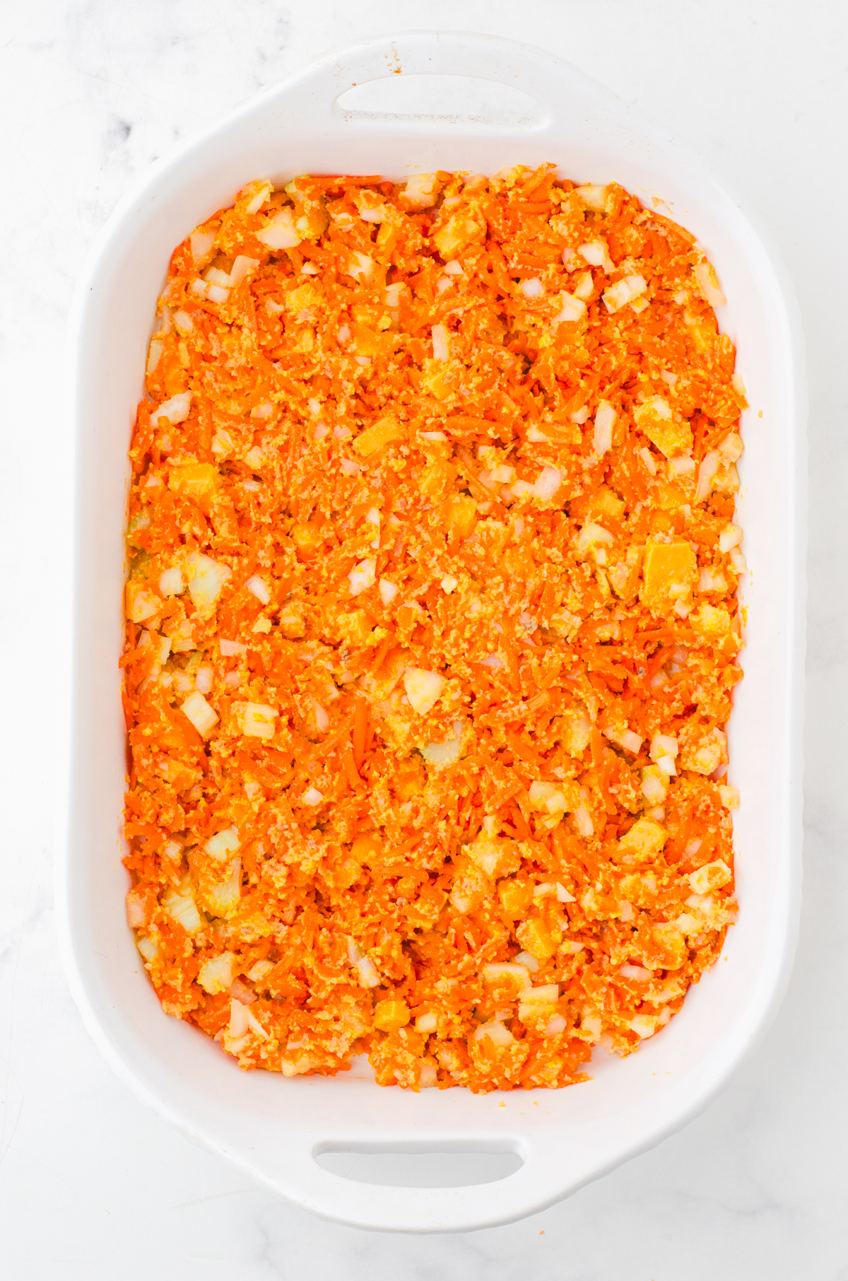 Shredded carrot casserole in a casserole dish ready to be baked.