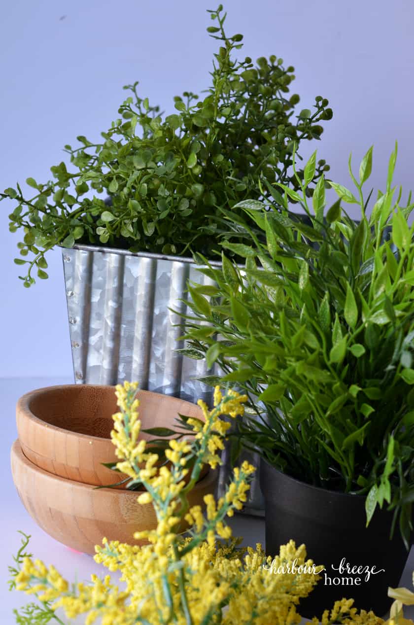 The supplies for this quick and simple DIY farmhouse centerpiece are an assortment of faux greenery and yellow flowers, along with a galvanized metal flower box.