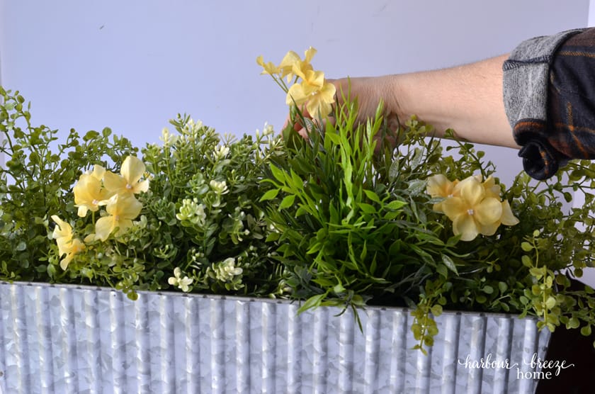 Place yellow flowers interspersed throughout the faux greenery.