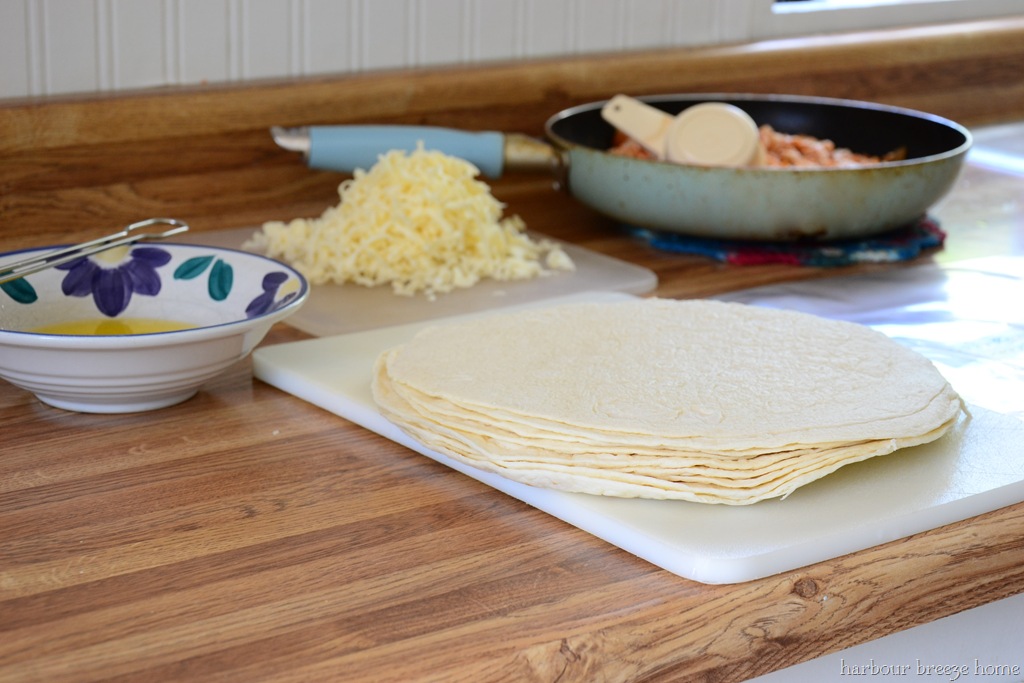 A stack of tortillas on the counter with a pan of cheese and stack of grated cheese behind it - the ingredients needed for this chicken chimichangas recipe.