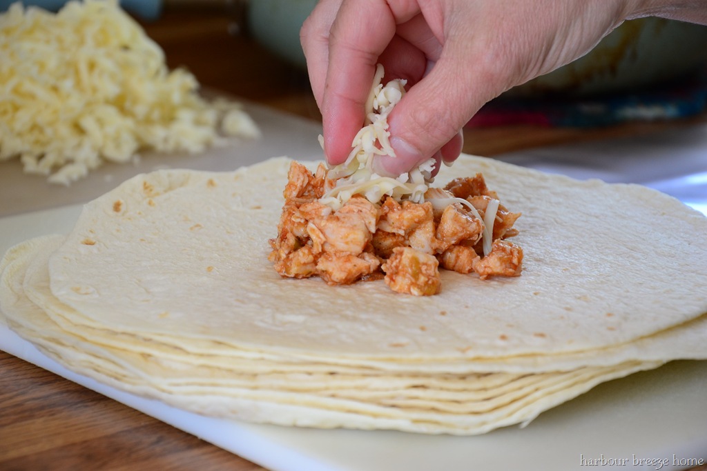 Cheese being piled on top of chicken mixure on a tortilla for this chicken chimicangas recipe.
