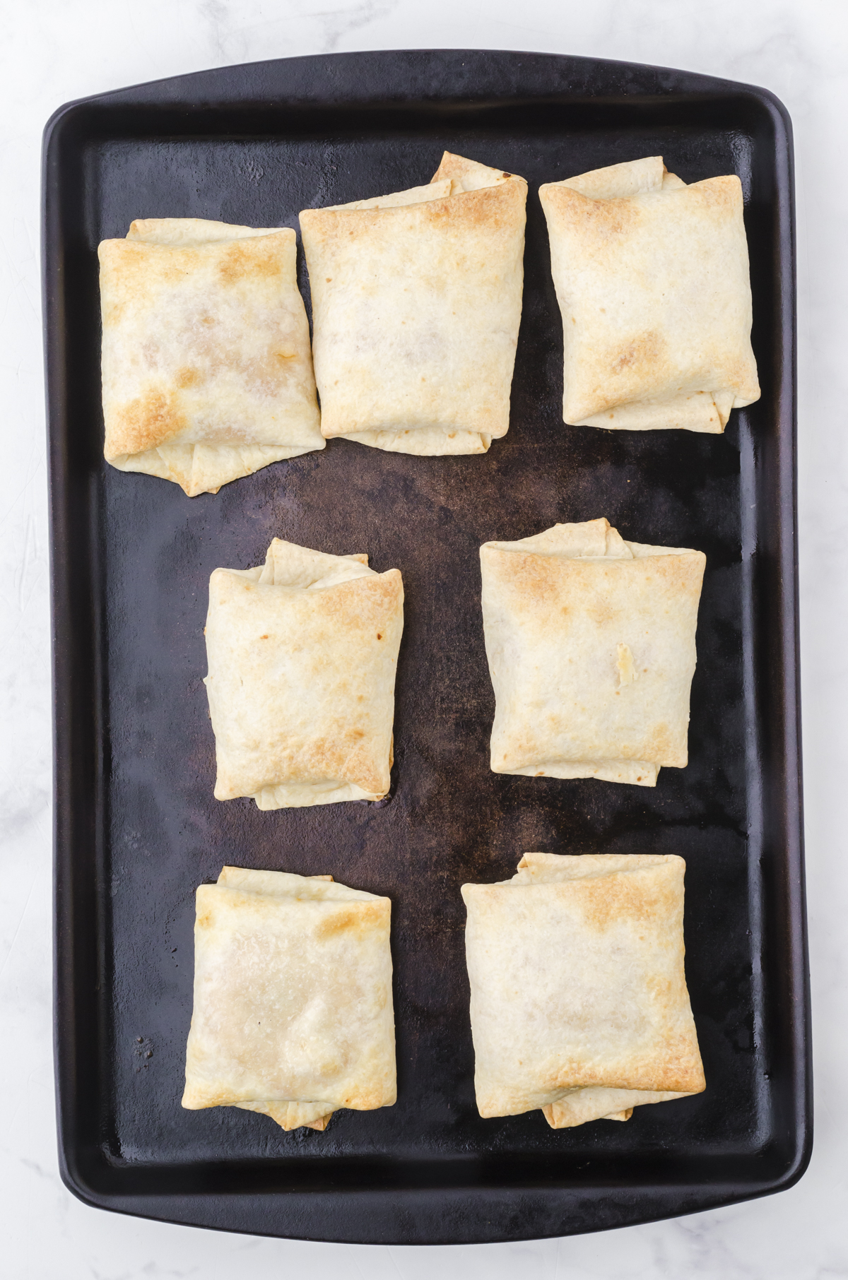 Baked chicken chimichangas on a baking sheet.