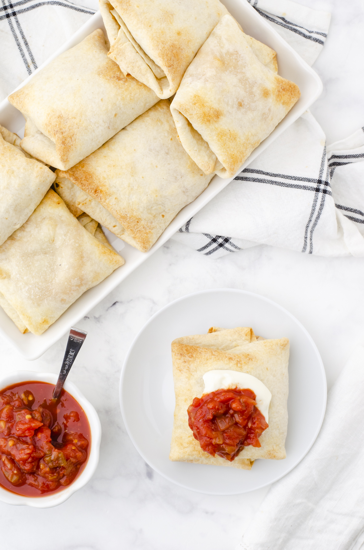A platter of stacked oven baked chicken chimichangas with a plate with one serving on it.