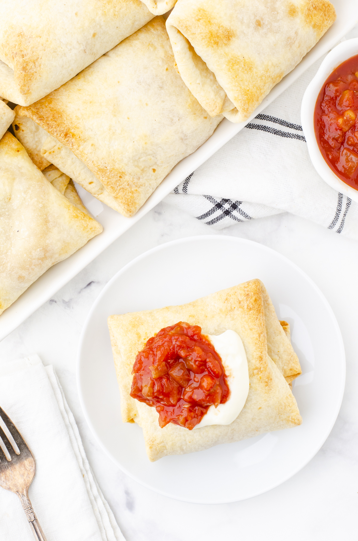 A plate with a chicken chimichanga on it with a bowl of salsa beside.