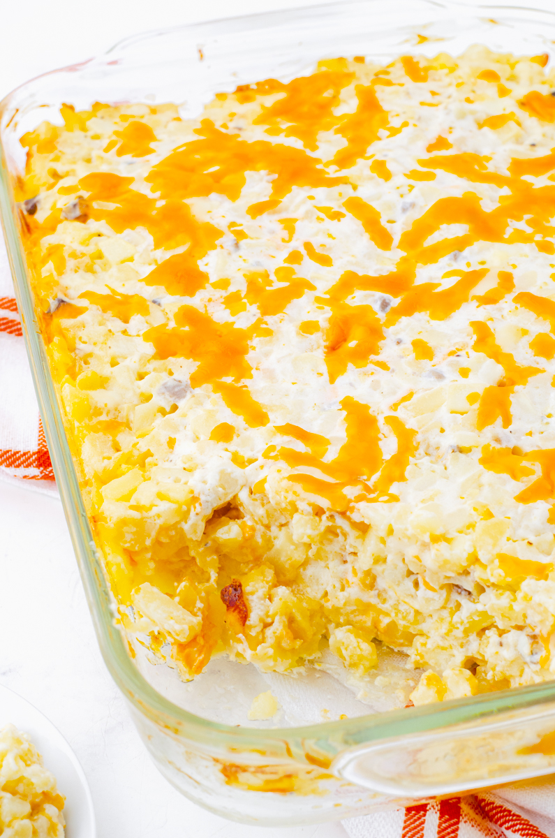 Baked cheesy potatoes casserole with hashbrowns with a serving dished out of the casserole dish.