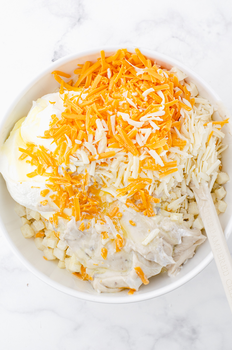 Ingredients for cheesy potatoes with frozen hashbrowns being mixed in a mixing bowl.