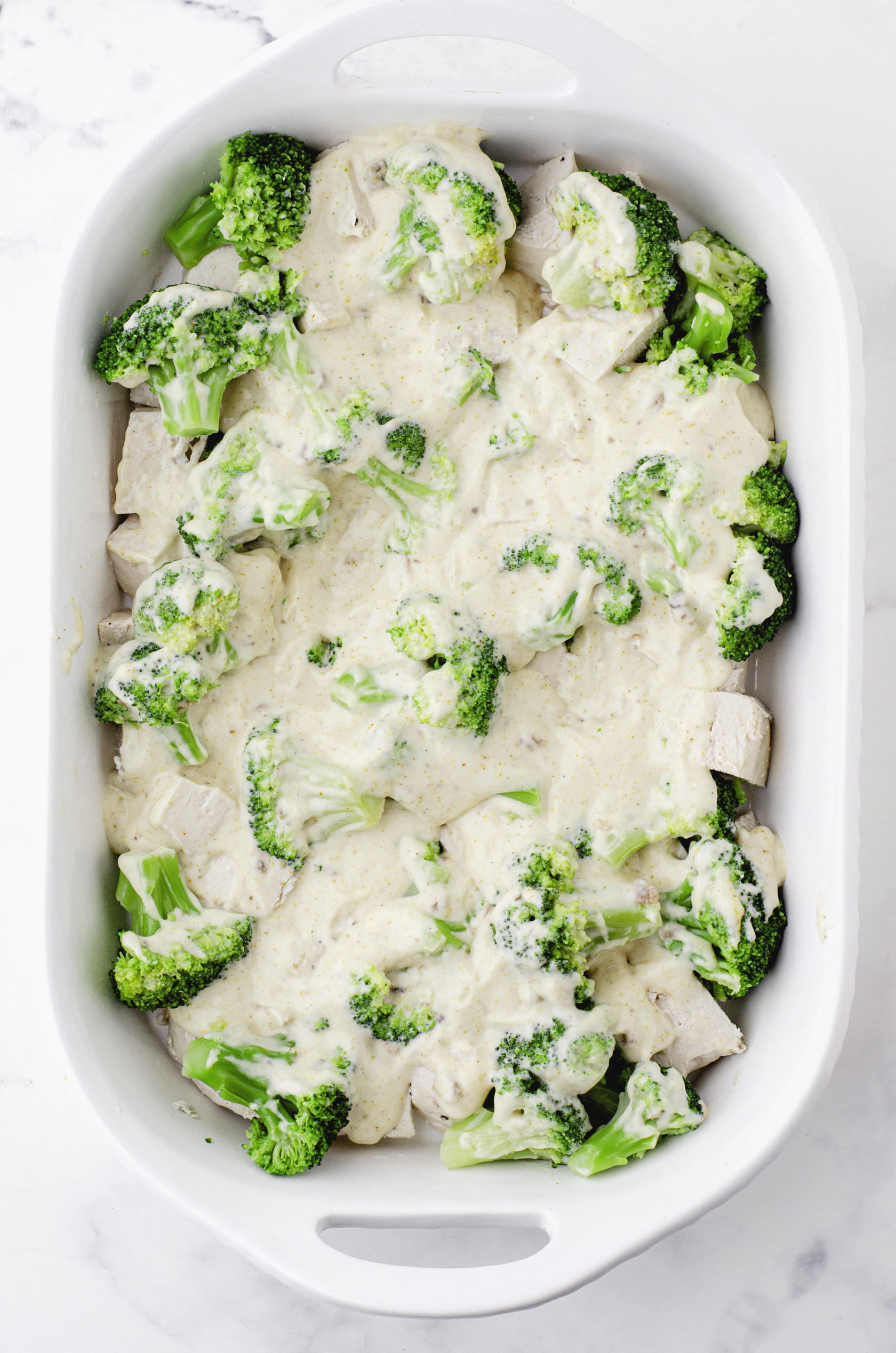 Chicken divan sauce poured over top of broccoli and chicken in baking dish for chicken divan casserole.