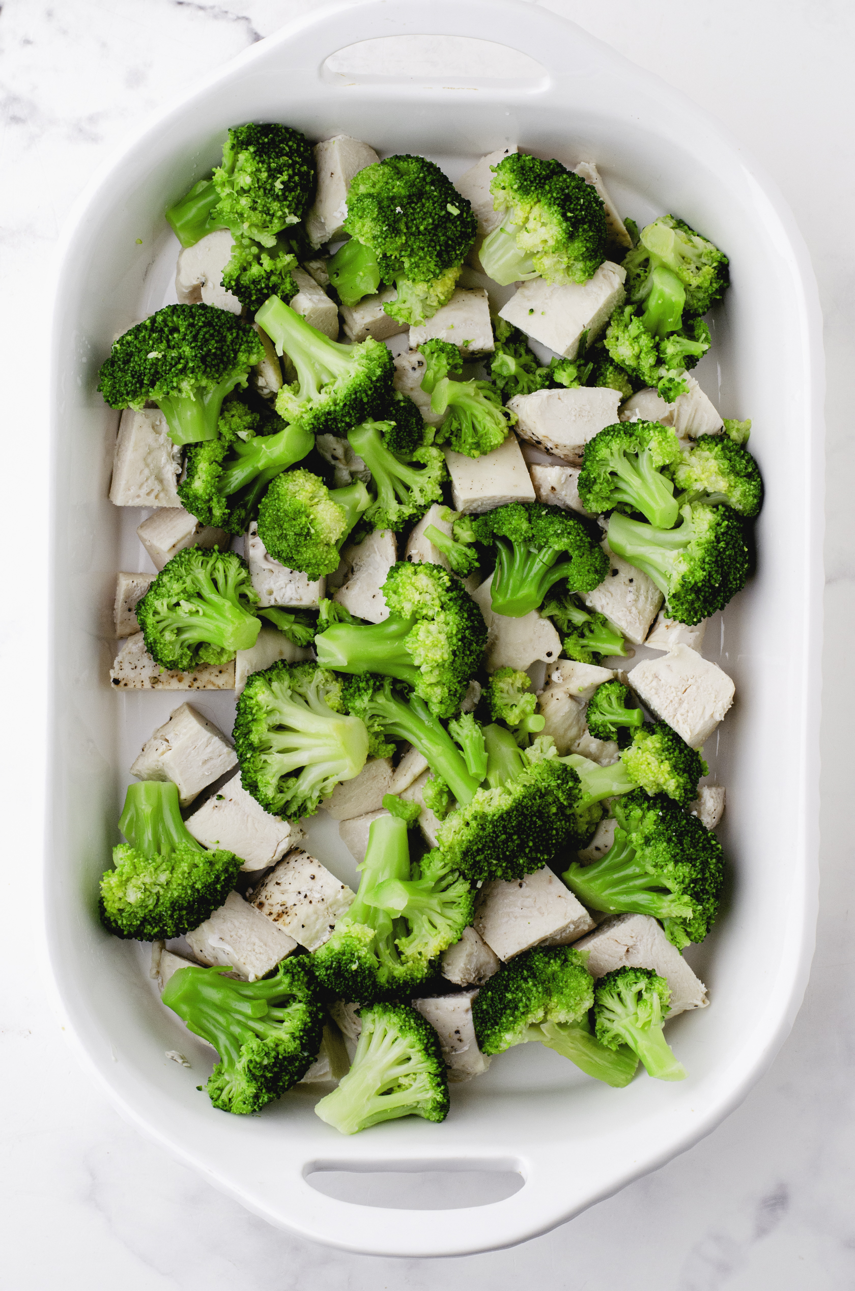 par-cooked broccoli layered over cooked chicken in casserole dish for chicken broccoli casserole