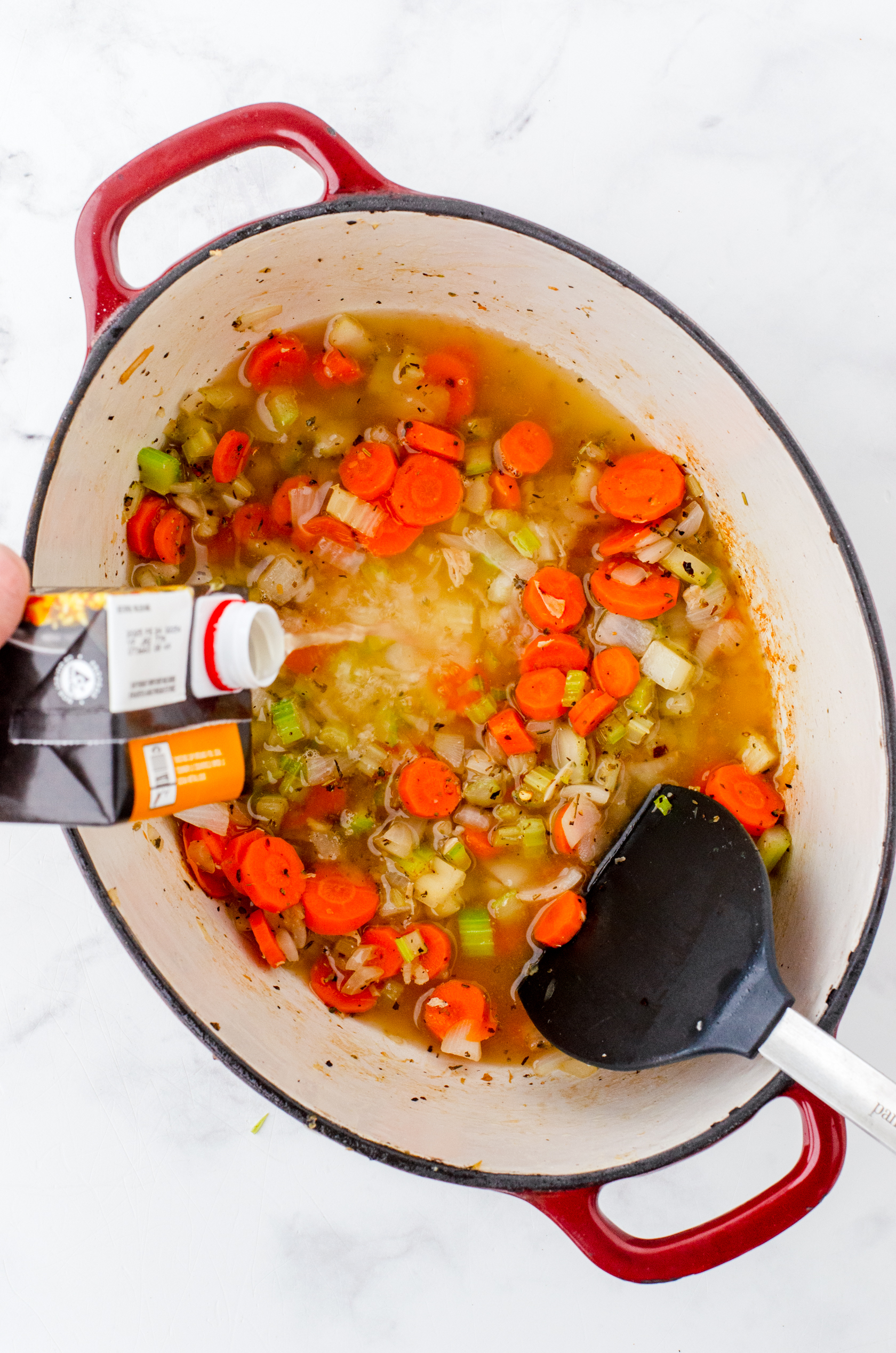 Chicken stock being poured into a pot of chicken noodle soup.
