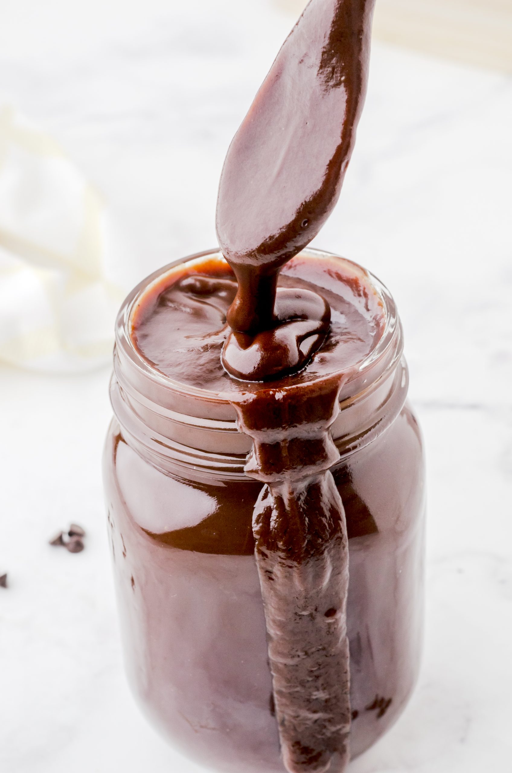 Homemade chocolate fudge sauce (hot fudge sauce) in a mason jar with a spoon drizzling the thick mixture into the top.
