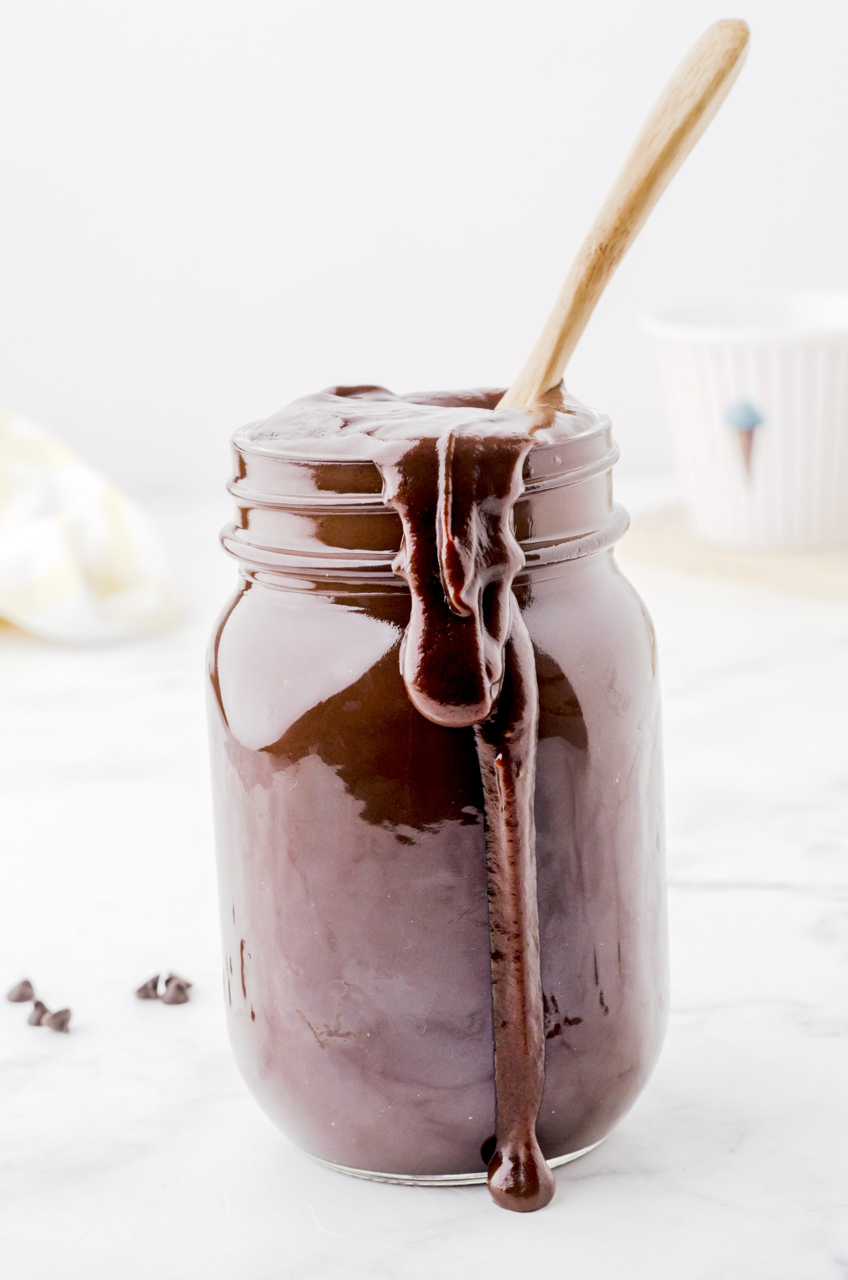 Homemade chocolate fudge sauce in a jar with a spoon in it
