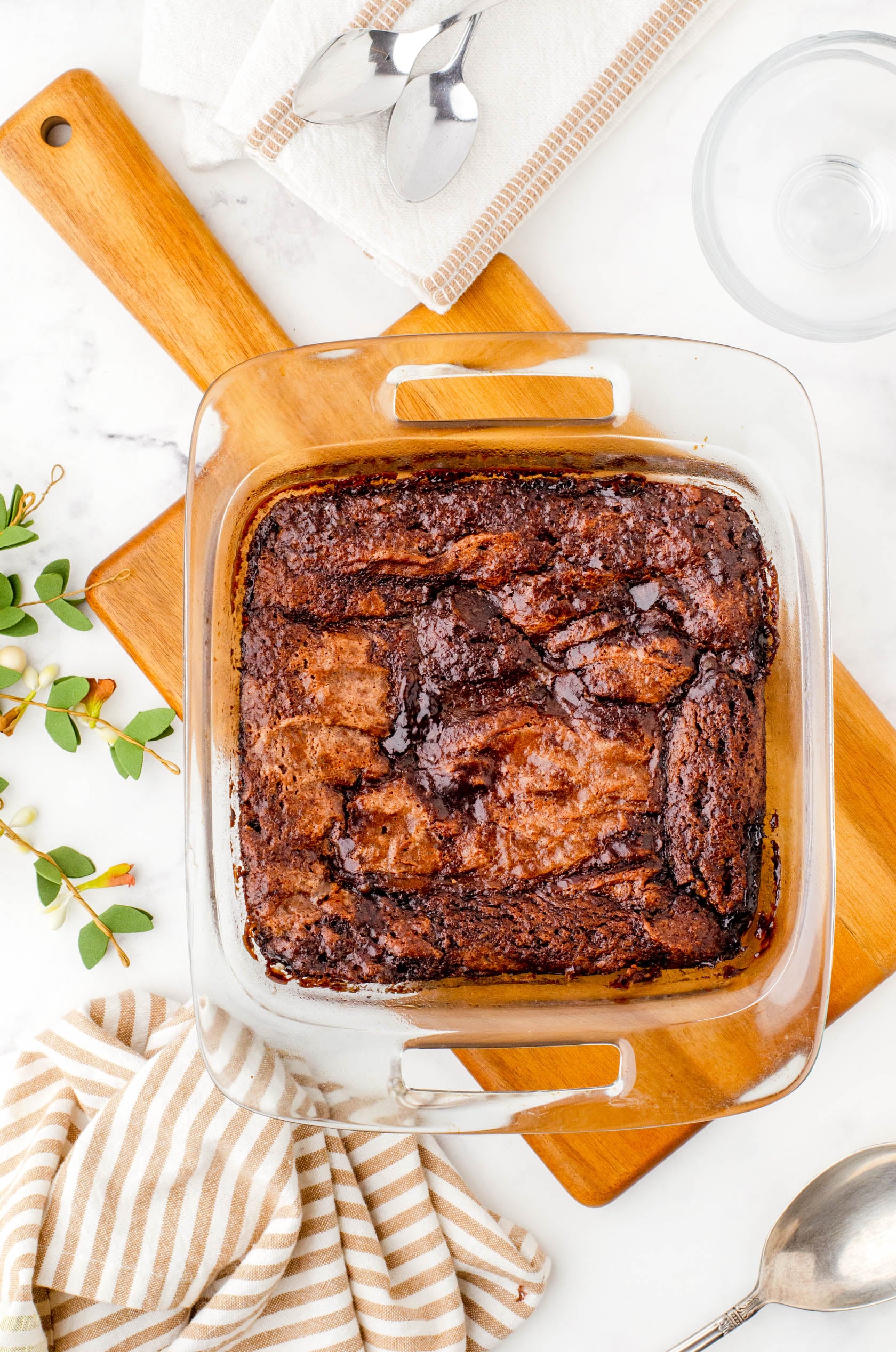 A pan of chocolate pudding cake baked and placed on a wooden cutting board while it cools.