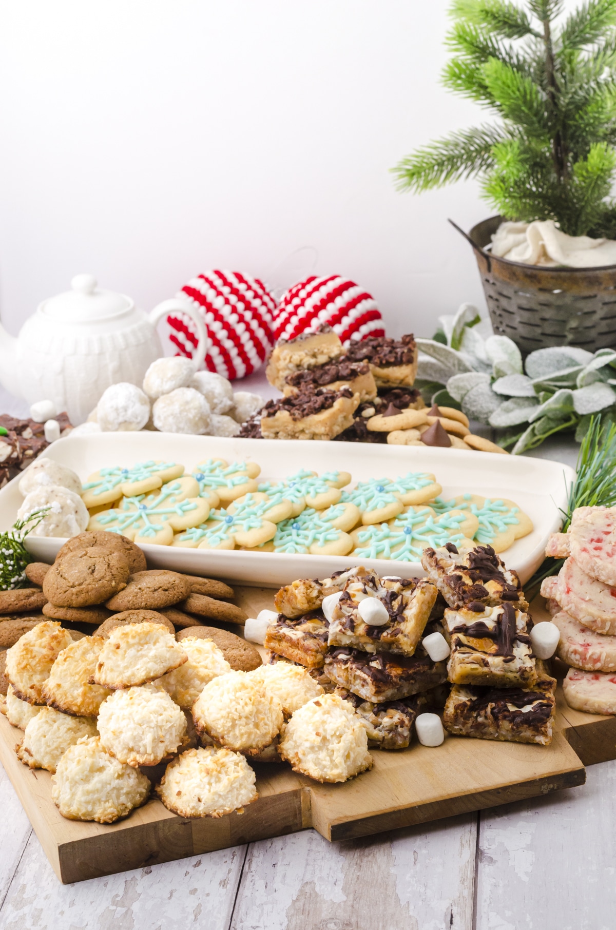 Coconut macaroons and gingersnaps piled on a flat wooden charcuterie board and sitting on a table.