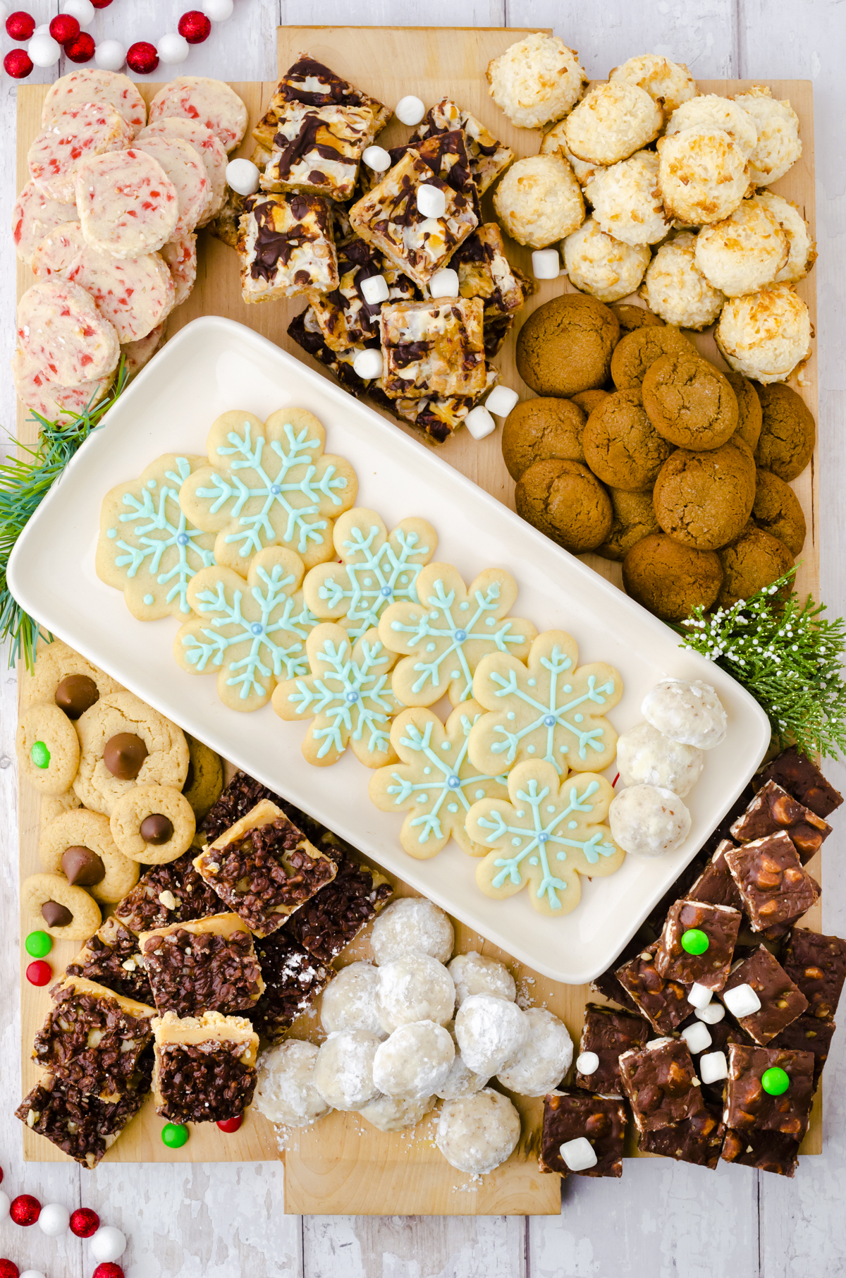 A platter of snowflake sugar cookies in the center of a large Christmas cookie charcuterie board with other cookies piled around it.