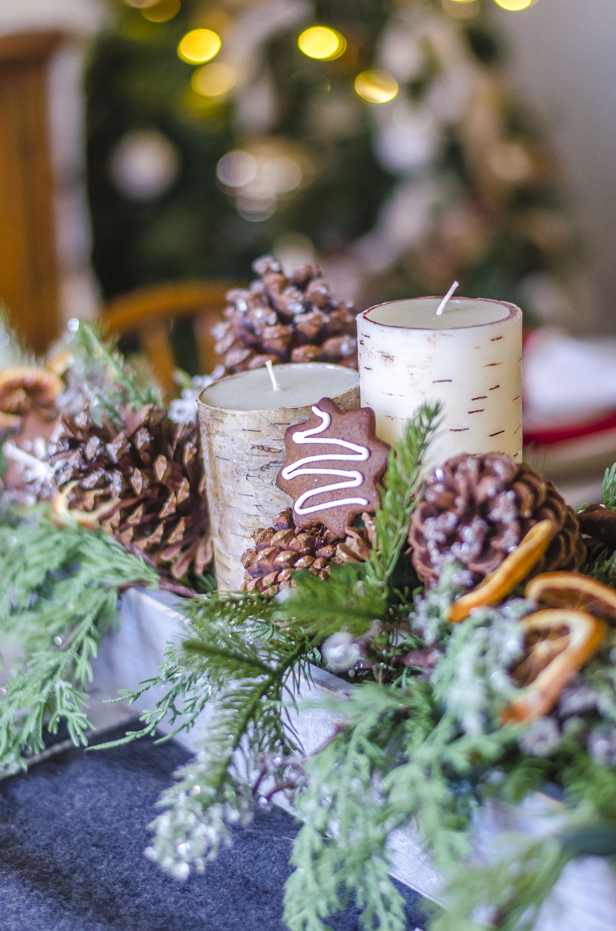Candles, pine cones, gingerbread cookies, dried orange slices, and faux greenery in a tray with Christmas tree lights in the background.