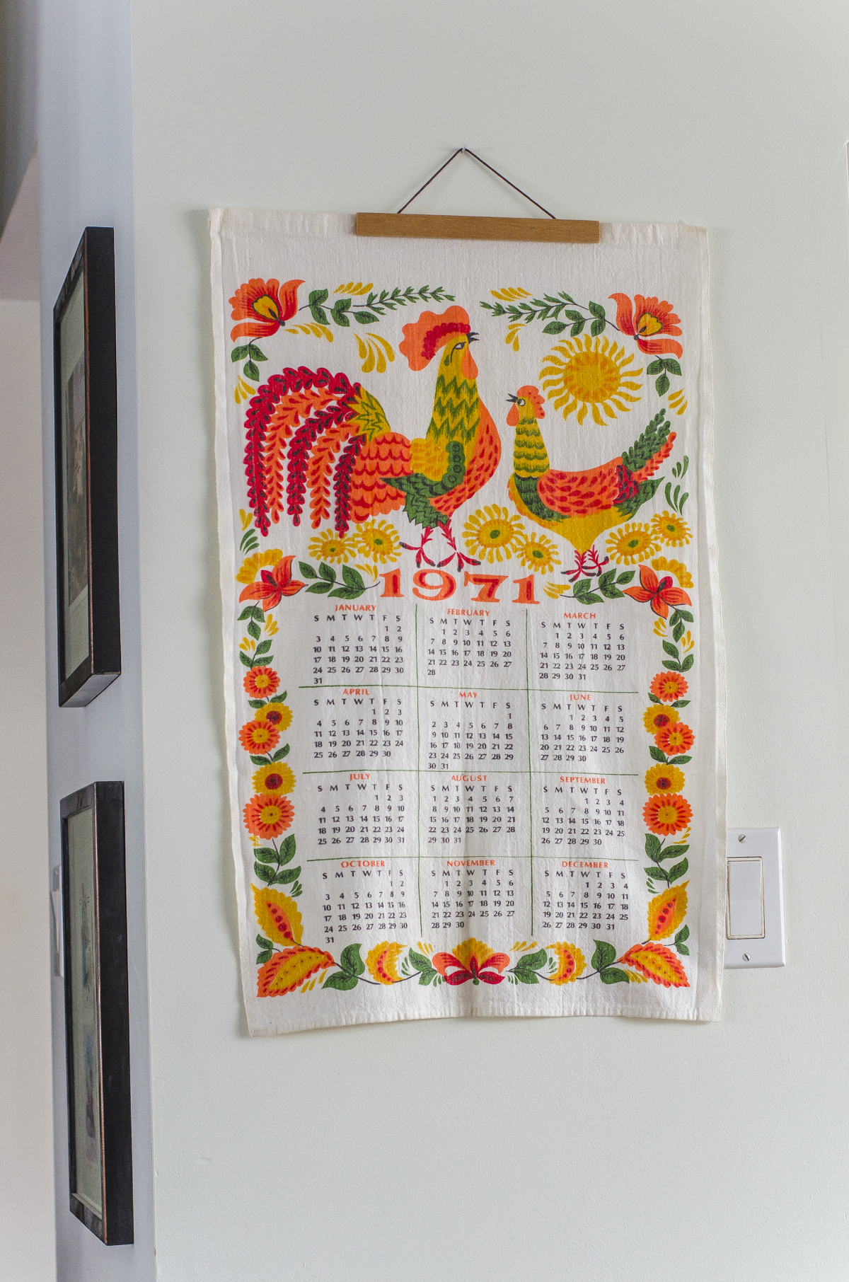 A dishtowel calendar with roosters from 1971 with the colors orange, mustard yellow and sage green. It's perfectly at home in a cottage core room!