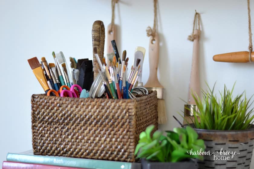 Basket of paintbrushes with greenery beside it