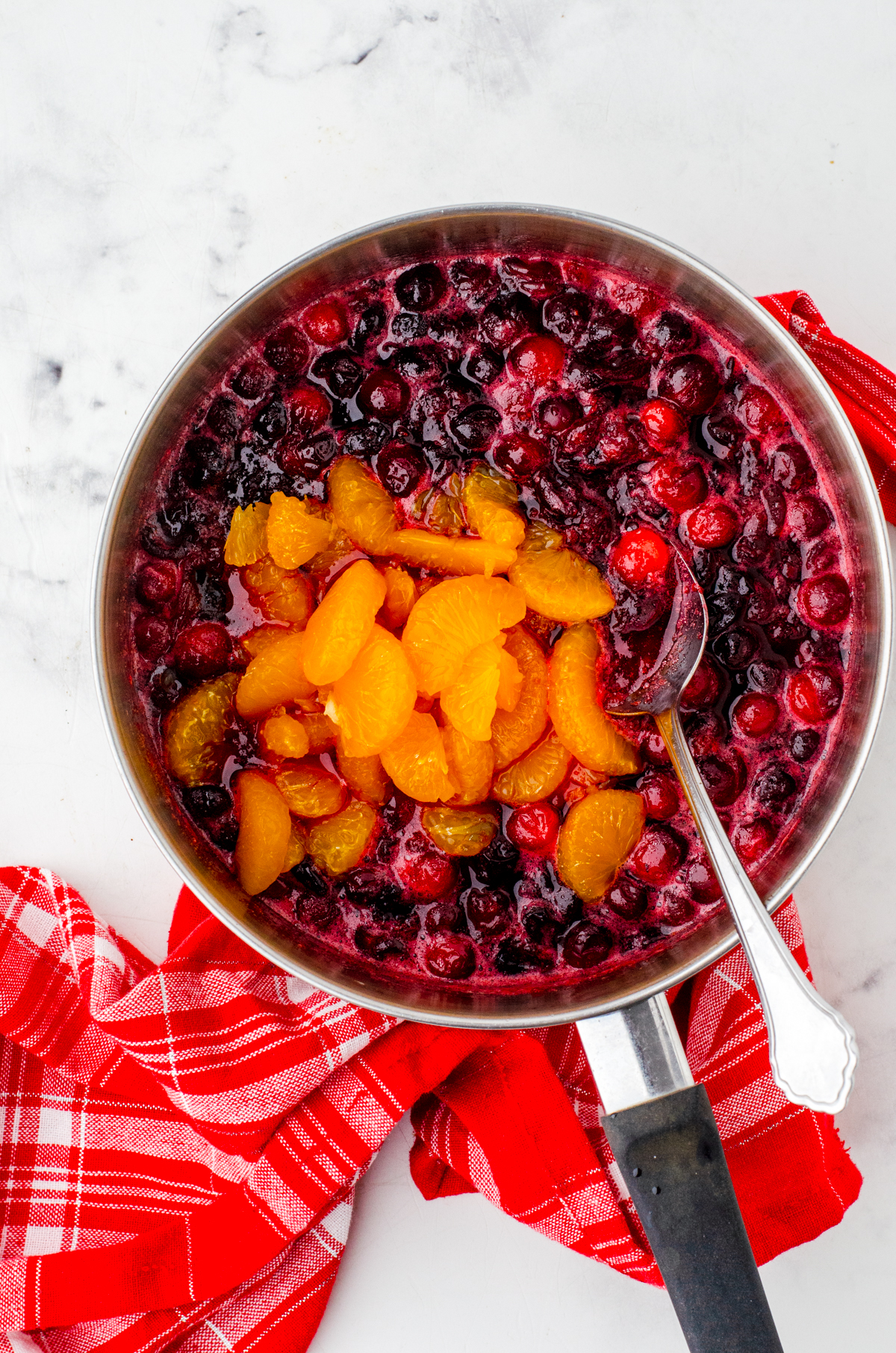 Mandarin oranges being added to partially cooked cranberries in a saucepan